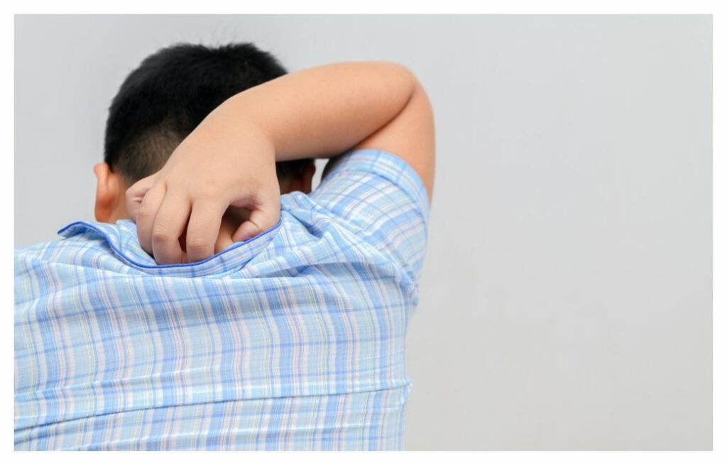 Young boy reaching behind his head to scratch his itchy neck. Photo taken from behind.