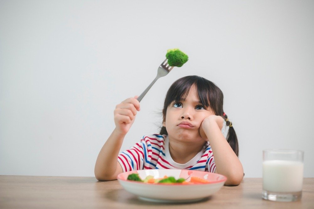 Little girl looking very unimpressed holding fork with a piece of brocoli