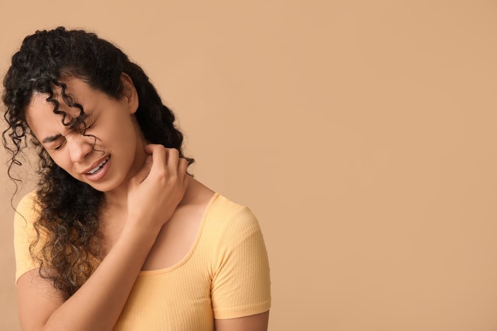 Young African-American woman with itchy skin scratching her neck. Her expression show how itchy her eczema is.
