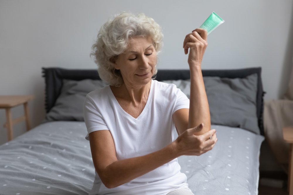 Older lady applying moisturiser to dry skin on her arms.