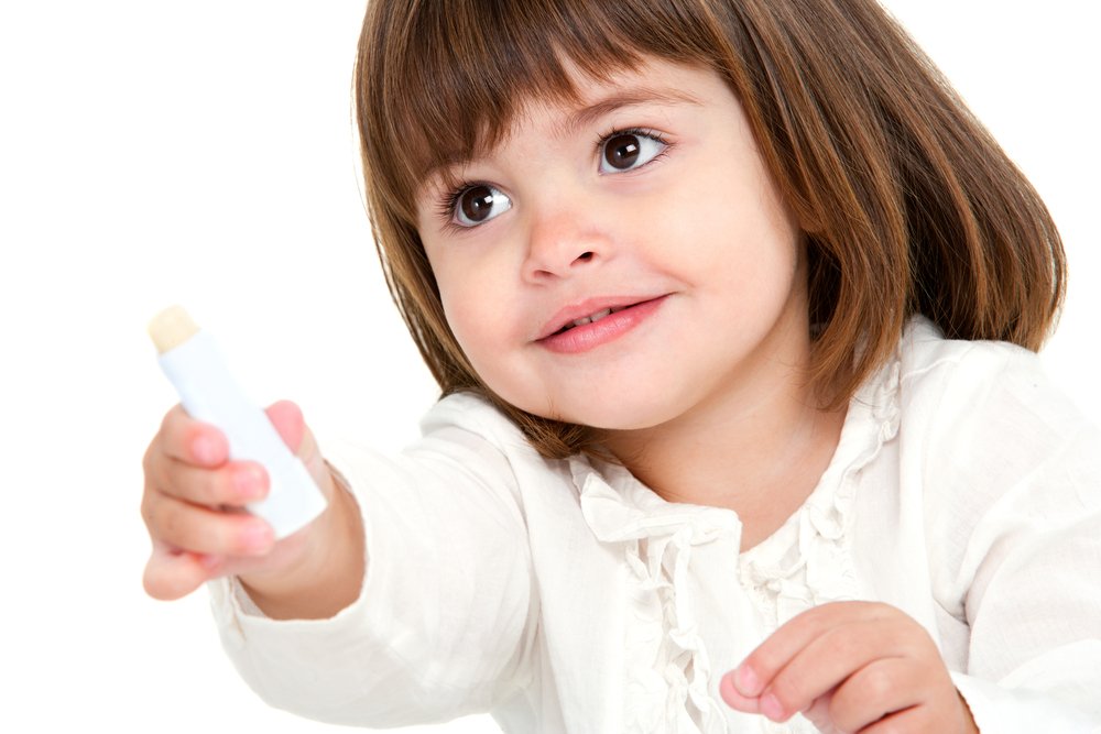 Little girl holding out an unbranded lip salve stick. Find tried and tested lip balm reviews in our blog